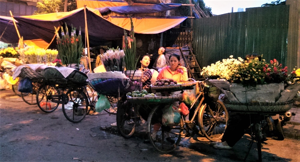 Two women selling flowers from their bicycles by the side of the road in Hanoi