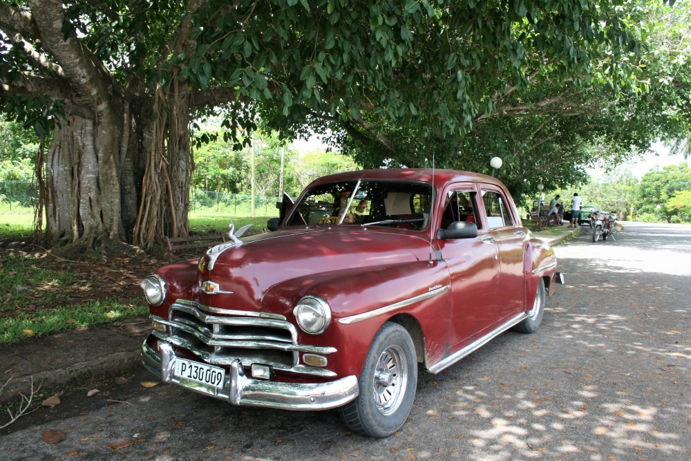 A dark red classic car by the side of a road in Cuba