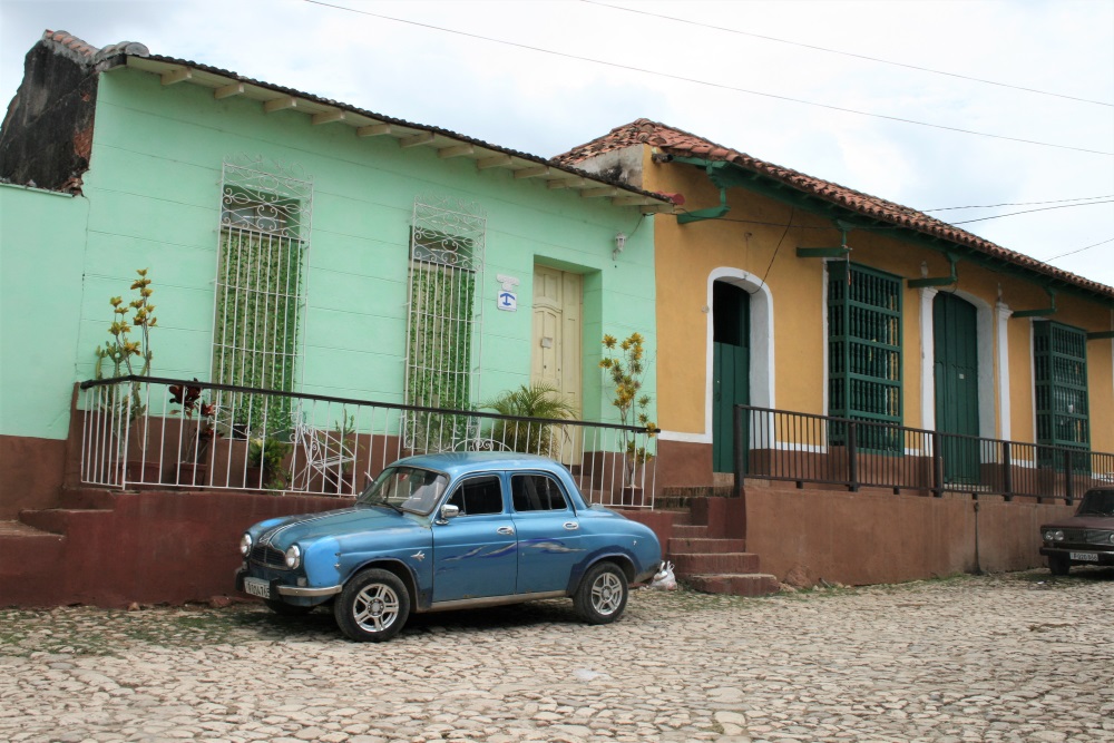 A blue classic car parked outside a house in Trinidad, Cuba